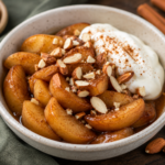 Warm cinnamon apples topped with chopped almonds and served with creamy yogurt in a ceramic bowl.