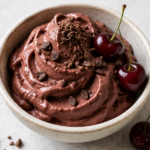 Creamy chocolate cherry nice cream topped with fresh cherries and chocolate shavings in a ceramic bowl.